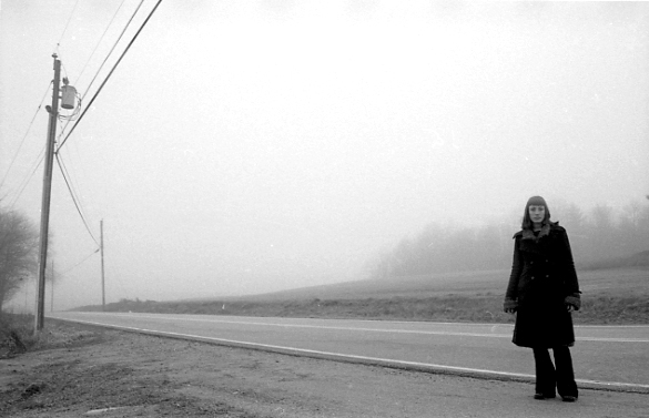 Jessica wearing all black, standing on a deserted misty road in New Hampshire.