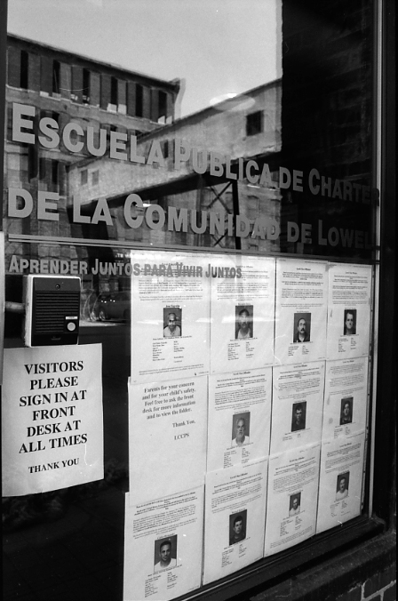 Black and white image of school window, with paper printouts showing photographs of local sex offenders.