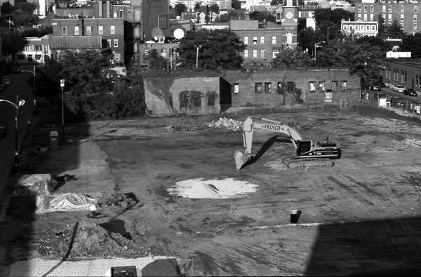 Black and white image of a demolished city block with a construction vehicle parked.