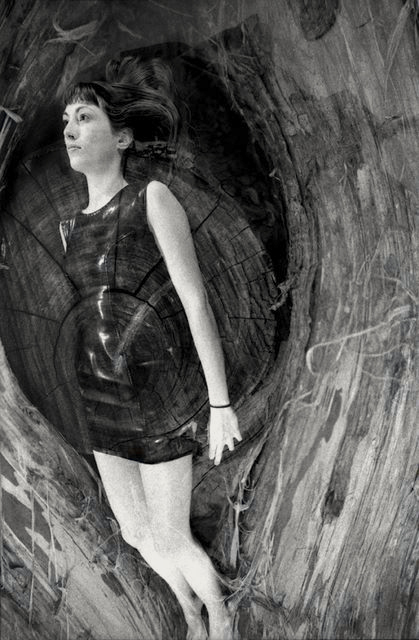 Black and white multiple exposure image of a woman floating on top of textured tree bark.