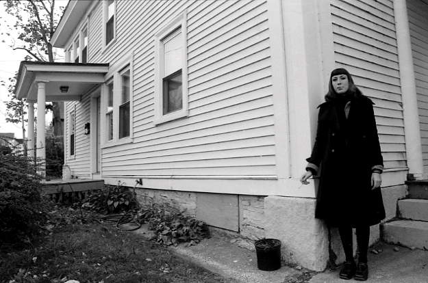 Jessica wearing all black, standing in front of a house in Lowell.