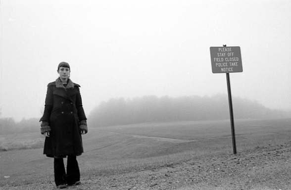 Jessica wearing all black, standing immediately in front of a large field with a sign that says 'Please stay off field'.