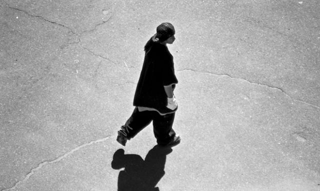 Black and white image of a young person with baggy pants walking across the road.