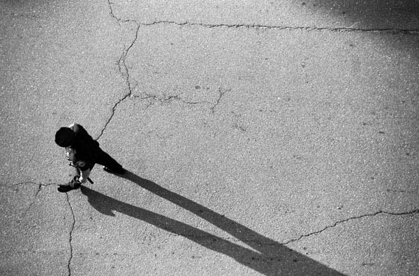 Black and white image of a policeman walking in the road with a long shadow.