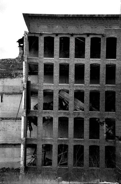 Black and white image of a brick wall in an old industrial building that's abandoned and falling apart.