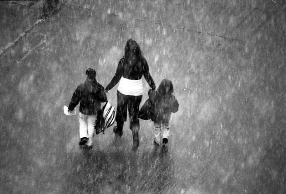 Black and white image of an adult and two children crossing the road.
