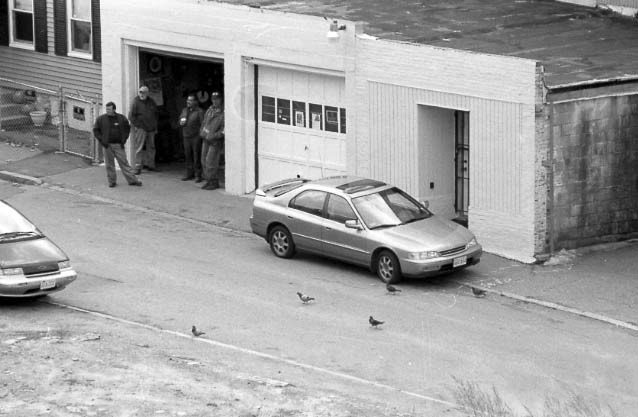 Black and white image of a group of men drinking coffee outside a garage.