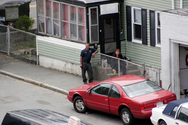 Color image of two people outside a house, watching the road.