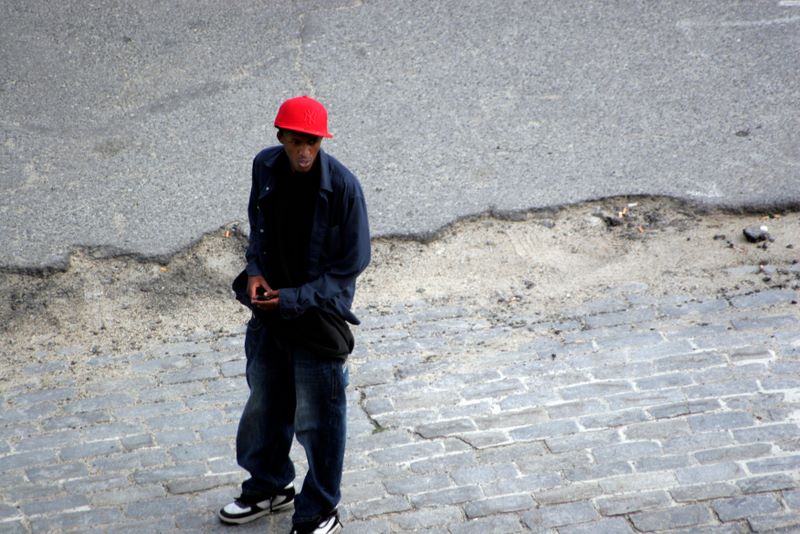 Color image of a man in a bright red hat standing in the road.