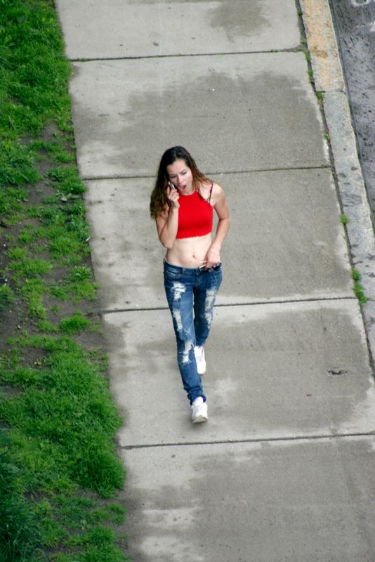 Color image of a woman in tight jeans and a belly shirt walking down the street talking on the phone.