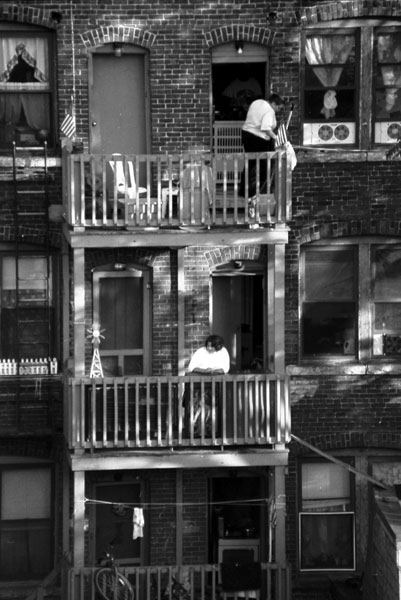 Black and white image of people on their porches, on multiple levels of an apartment building.